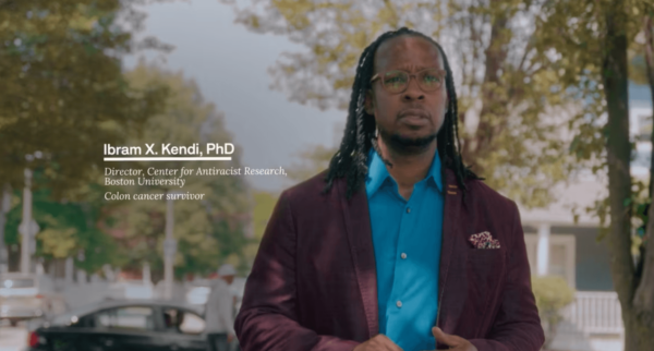 Dr. ibram x. kendi, wearing glasses and a maroon blazer, stands outdoors as identified as director at boston university and a colon cancer survivor.